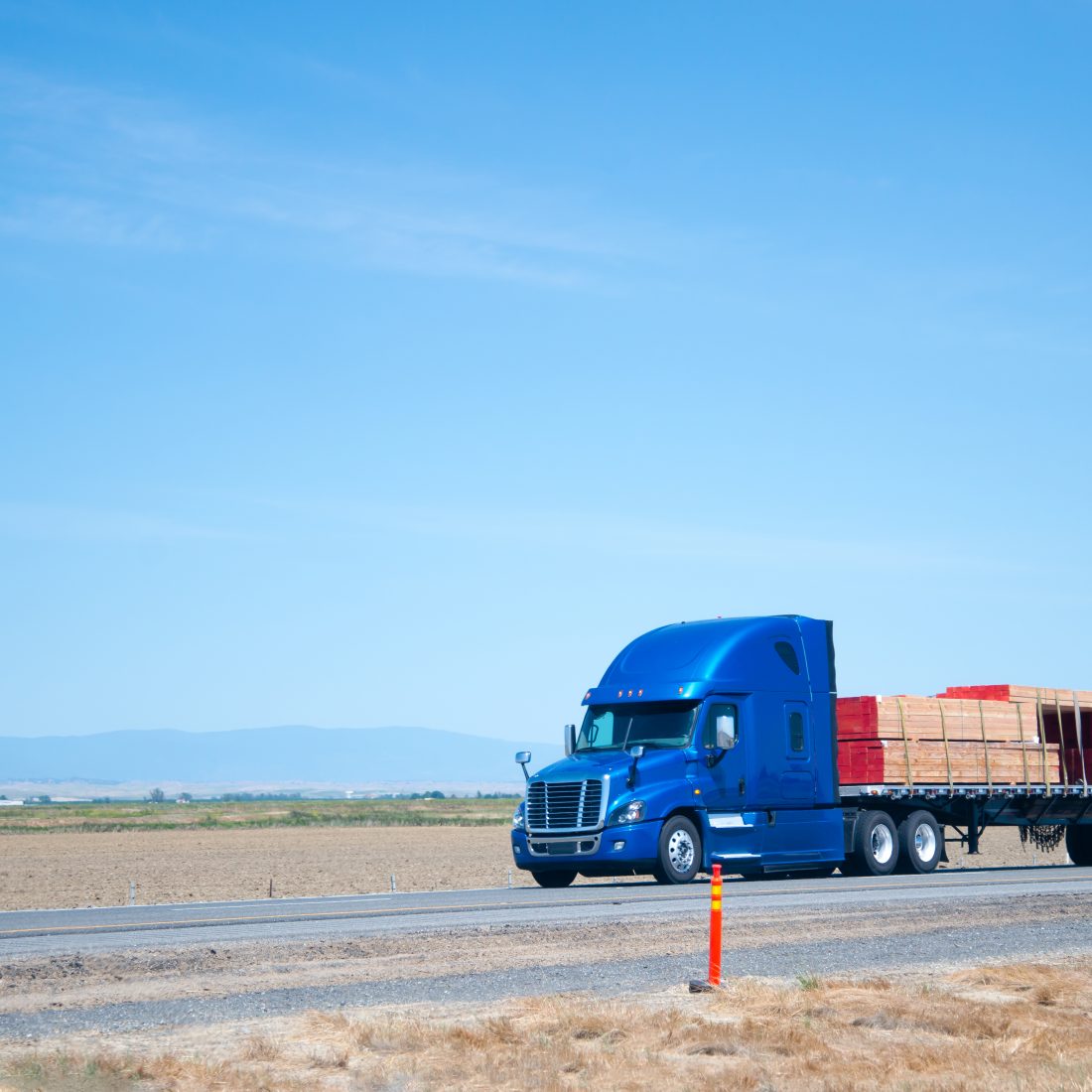 Big rig blue semi truck with flat bed trailer transporting lumber wood ...